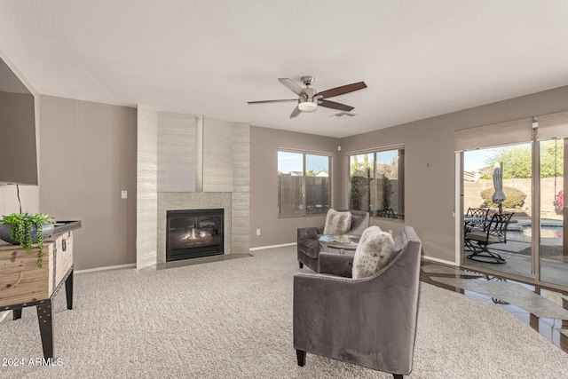 living room featuring ceiling fan, light colored carpet, a textured ceiling, and a tiled fireplace