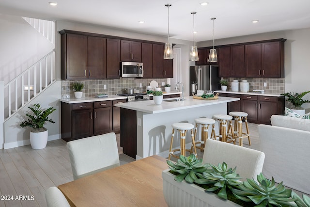 kitchen featuring a sink, light countertops, appliances with stainless steel finishes, an island with sink, and decorative light fixtures