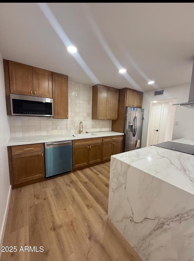 kitchen featuring tasteful backsplash, sink, stainless steel appliances, light stone countertops, and light hardwood / wood-style flooring