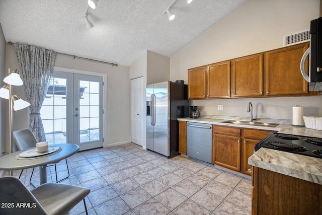 kitchen with lofted ceiling, french doors, sink, light tile patterned floors, and stainless steel appliances