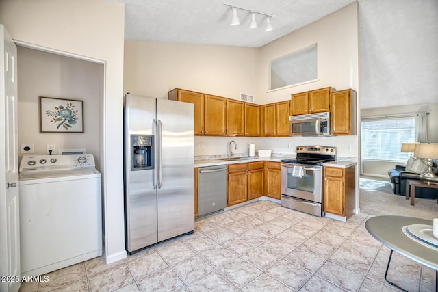 kitchen with sink, a textured ceiling, washer / dryer, light tile patterned floors, and appliances with stainless steel finishes