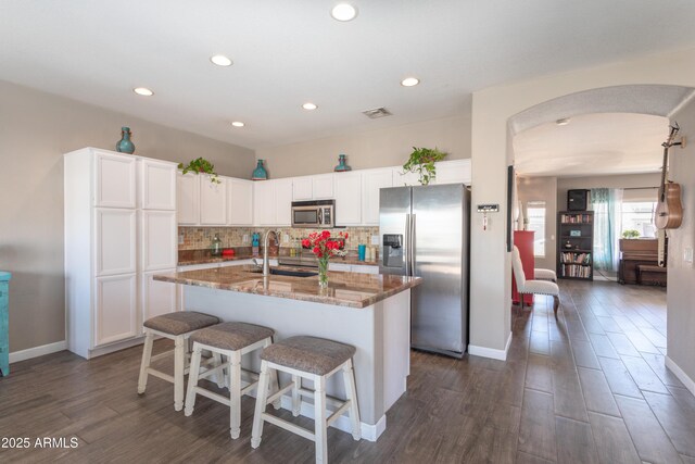 kitchen with stone counters, visible vents, appliances with stainless steel finishes, arched walkways, and a sink