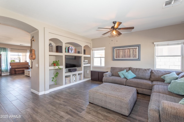 living area featuring arched walkways, dark wood finished floors, visible vents, and ceiling fan
