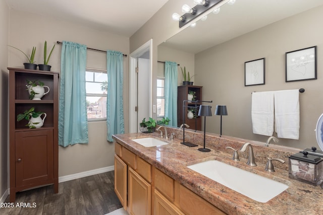 full bathroom featuring wood finished floors, double vanity, a sink, and baseboards