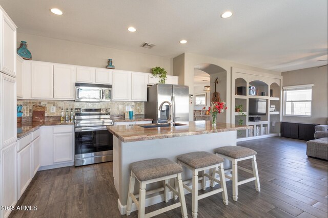 kitchen featuring open floor plan, appliances with stainless steel finishes, a kitchen breakfast bar, light stone countertops, and backsplash