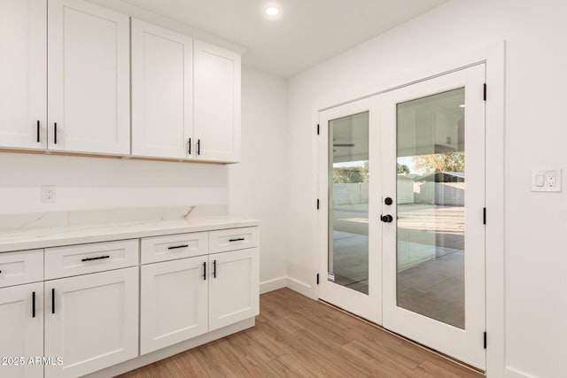 kitchen with light stone counters, light hardwood / wood-style floors, white cabinets, and french doors