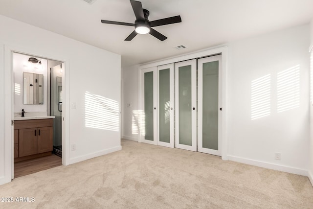 unfurnished bedroom featuring connected bathroom, sink, a closet, ceiling fan, and light colored carpet