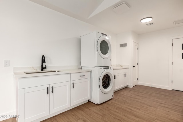 laundry room with cabinets, sink, stacked washer and dryer, and light wood-type flooring