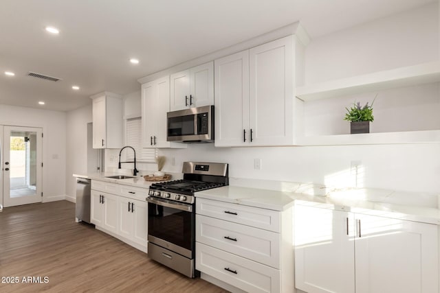 kitchen with sink, light wood-type flooring, white cabinetry, light stone countertops, and stainless steel appliances