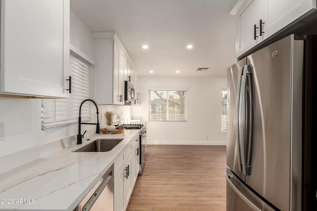 kitchen featuring appliances with stainless steel finishes, white cabinetry, sink, light hardwood / wood-style flooring, and light stone counters