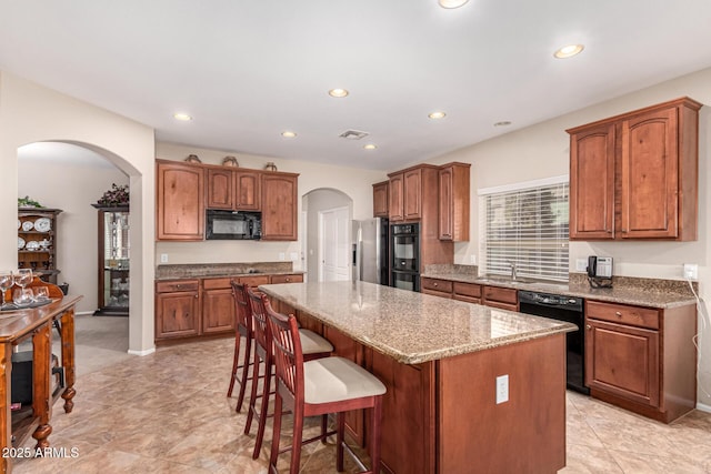 kitchen featuring sink, a breakfast bar area, a center island, light stone counters, and black appliances