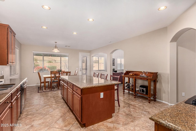 kitchen featuring a kitchen island, pendant lighting, dishwashing machine, a kitchen breakfast bar, and light stone countertops