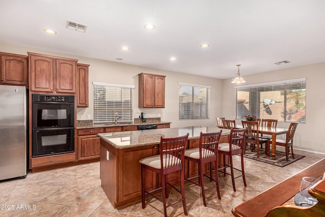 kitchen featuring a kitchen bar, hanging light fixtures, a kitchen island, light stone countertops, and black appliances