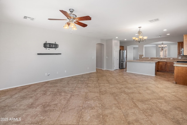 unfurnished living room featuring a sink, visible vents, ceiling fan with notable chandelier, and arched walkways