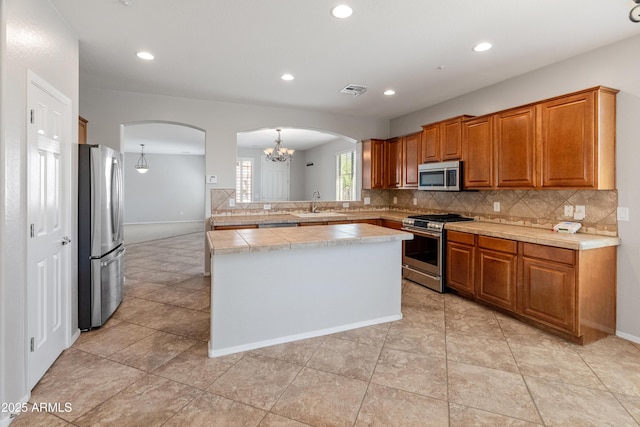 kitchen with decorative backsplash, appliances with stainless steel finishes, a center island, arched walkways, and brown cabinetry