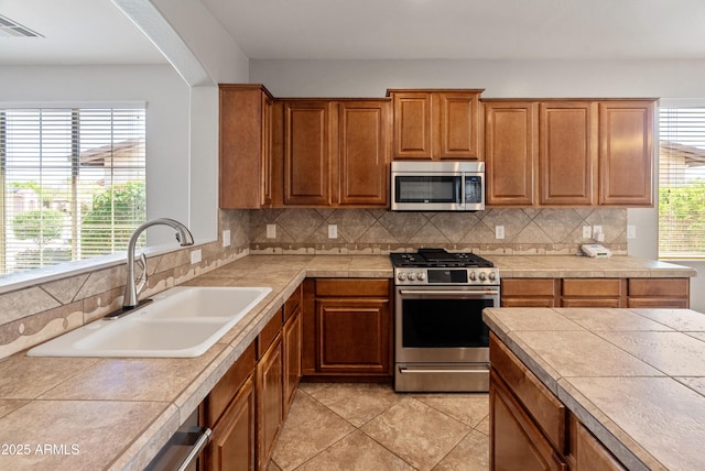 kitchen featuring decorative backsplash, stainless steel appliances, brown cabinets, a sink, and visible vents