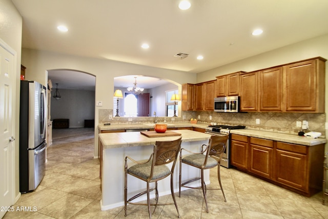 kitchen with appliances with stainless steel finishes, backsplash, a kitchen island, a kitchen bar, and decorative light fixtures