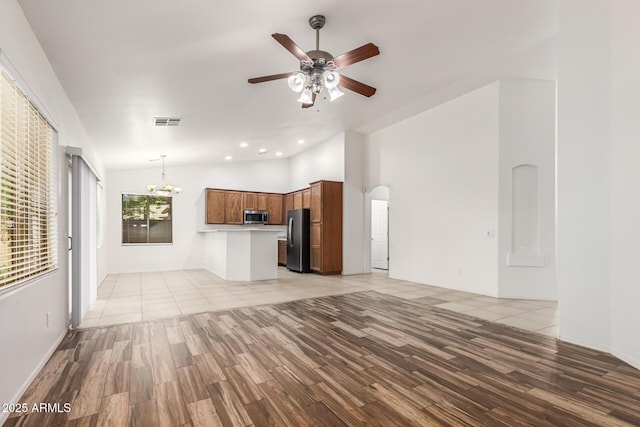 unfurnished living room featuring ceiling fan with notable chandelier, high vaulted ceiling, and light hardwood / wood-style flooring