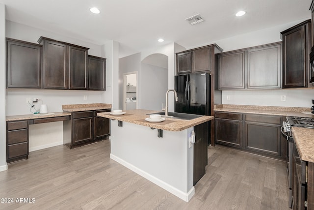 kitchen with a center island with sink, black refrigerator, sink, stainless steel gas range, and light hardwood / wood-style floors