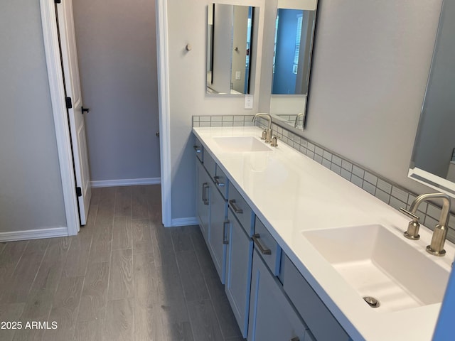 bathroom with wood finished floors, double vanity, baseboards, and tasteful backsplash