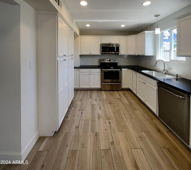 kitchen featuring white cabinets, stainless steel appliances, light hardwood / wood-style flooring, and hanging light fixtures