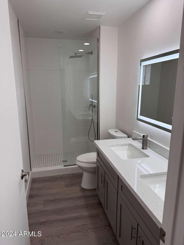 bathroom with tiled shower, vanity, wood-type flooring, and toilet