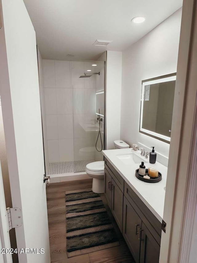 bathroom featuring hardwood / wood-style flooring, vanity, toilet, and a tile shower