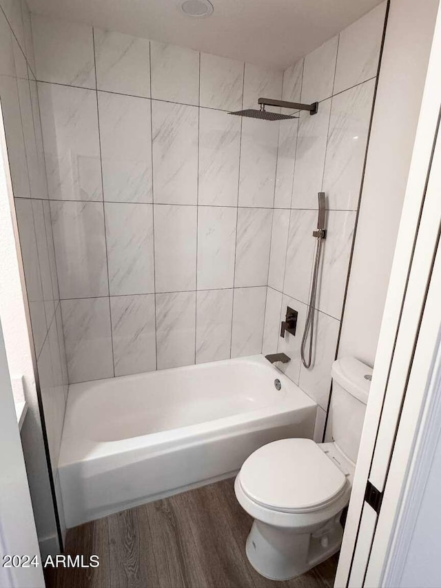 bathroom with hardwood / wood-style flooring, toilet, and tiled shower / bath