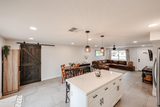 kitchen with light stone counters, visible vents, a barn door, open floor plan, and white cabinets