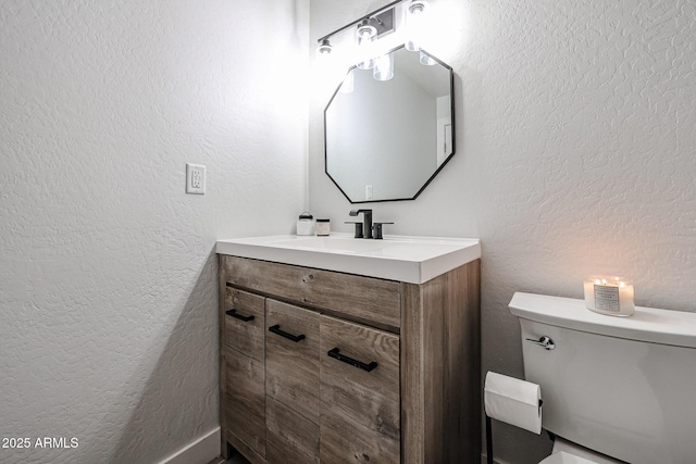 half bath with a textured wall, vanity, and toilet