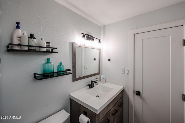 half bathroom featuring a textured wall, vanity, and toilet