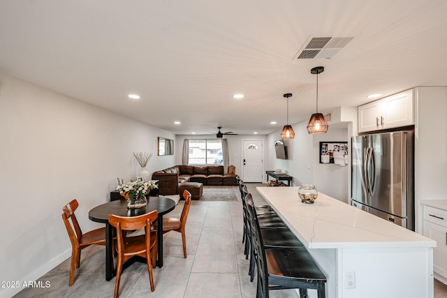 kitchen with light tile patterned flooring, a kitchen island, visible vents, white cabinets, and freestanding refrigerator