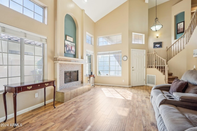 living room featuring light wood-type flooring, a tile fireplace, and a towering ceiling