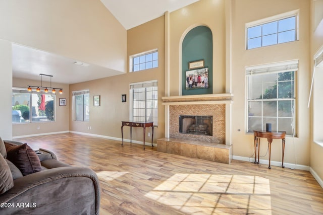 living room featuring plenty of natural light, a towering ceiling, a tile fireplace, and light hardwood / wood-style flooring