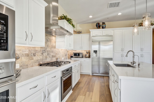 kitchen featuring wall chimney range hood, sink, hanging light fixtures, white cabinetry, and stainless steel appliances