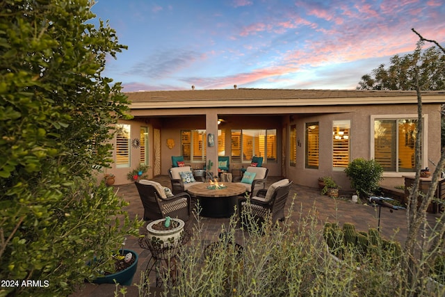 back of house at dusk featuring a patio area, an outdoor living space with a fire pit, and stucco siding