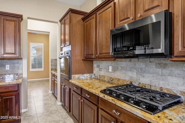 kitchen featuring light stone counters, stainless steel appliances, backsplash, light tile patterned flooring, and baseboards