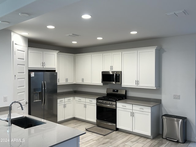 kitchen with white cabinets, appliances with stainless steel finishes, light stone countertops, light hardwood / wood-style flooring, and sink