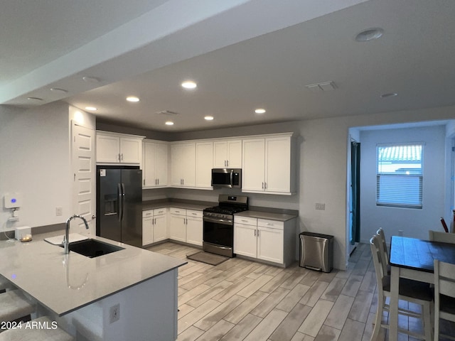 kitchen with sink, light wood-type flooring, kitchen peninsula, stainless steel appliances, and white cabinets