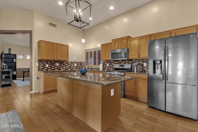 kitchen with appliances with stainless steel finishes, dark stone counters, pendant lighting, a high ceiling, and a kitchen island