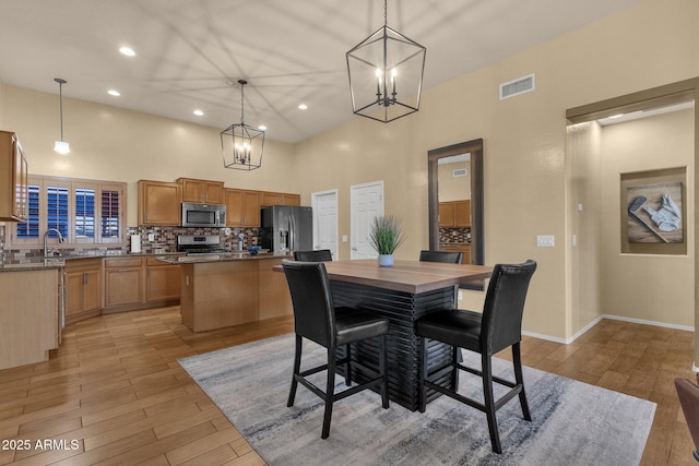 dining space with a high ceiling, light hardwood / wood-style floors, a notable chandelier, and sink