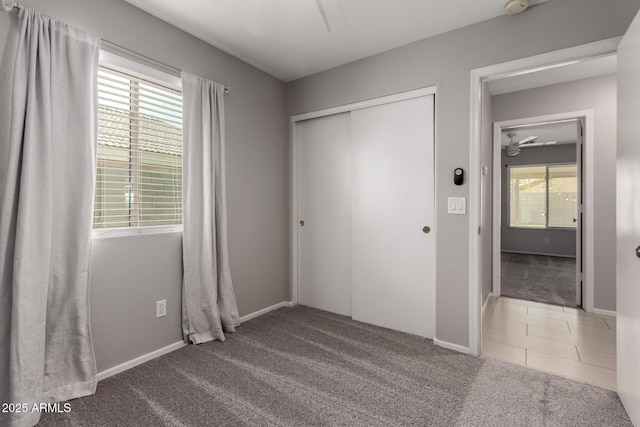 unfurnished bedroom with carpet floors, a closet, baseboards, and tile patterned floors