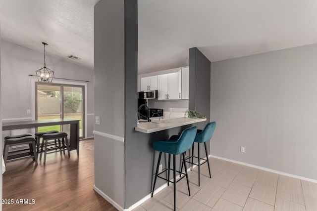 kitchen with a sink, white cabinetry, a kitchen breakfast bar, stainless steel microwave, and an inviting chandelier