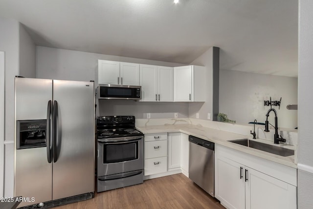 kitchen with appliances with stainless steel finishes, white cabinets, a sink, and wood finished floors