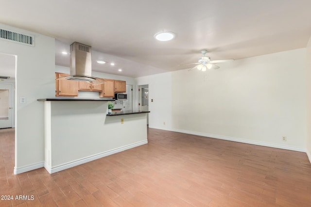 kitchen featuring kitchen peninsula, island range hood, ceiling fan, light brown cabinets, and light hardwood / wood-style floors