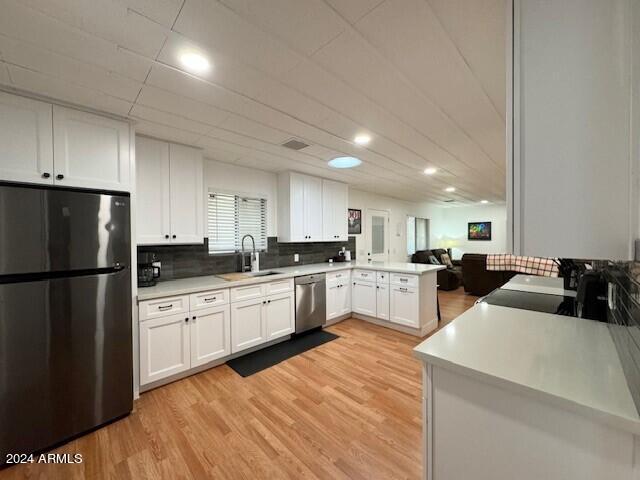 kitchen featuring kitchen peninsula, appliances with stainless steel finishes, light hardwood / wood-style flooring, white cabinets, and sink