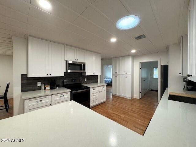 kitchen with white cabinets, refrigerator, hardwood / wood-style floors, backsplash, and range with electric cooktop