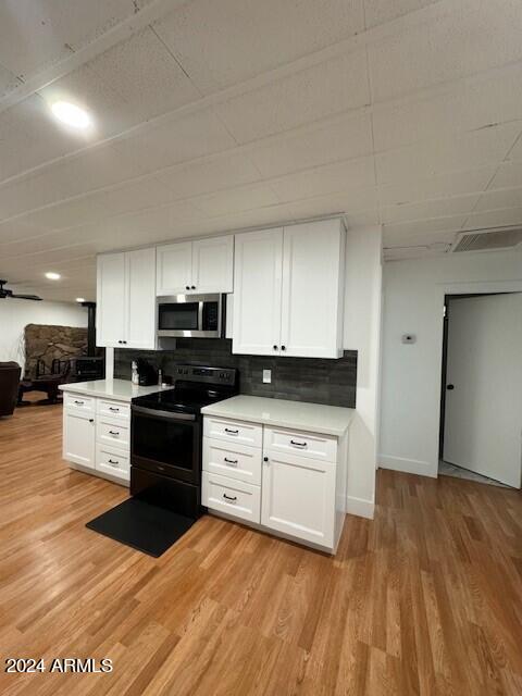 kitchen with electric range, light hardwood / wood-style flooring, tasteful backsplash, and white cabinets