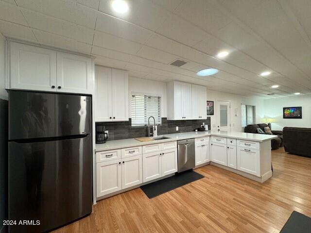 kitchen with white cabinets, light hardwood / wood-style flooring, backsplash, appliances with stainless steel finishes, and sink