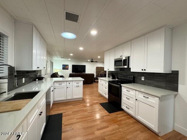 kitchen featuring white cabinetry, backsplash, kitchen peninsula, appliances with stainless steel finishes, and light hardwood / wood-style floors